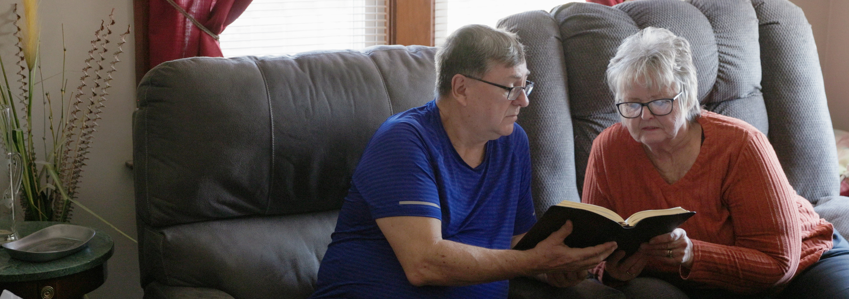 Foster parents sit on the couch, reading their Bible